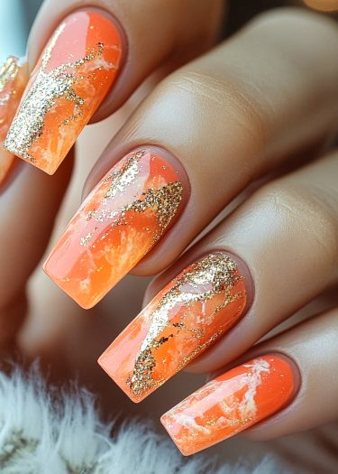 Vibrant orange nails with gold foil and marble design for a chic, luxurious look.