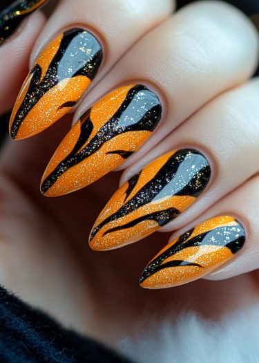 Vibrant orange nail art with black stripes and sparkling glitter for a bold, stylish look.