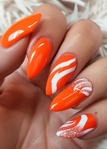 Vivid orange almond-shaped nails with glossy finish and dynamic white wave designs.