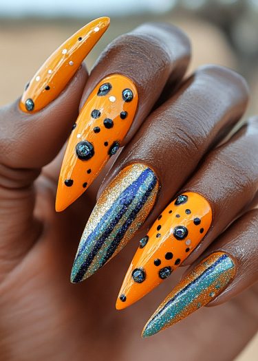 Vibrant orange nail art featuring glossy black polka dots and dazzling glitter accents.