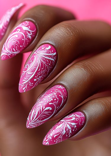 Vibrant pink stiletto nails with intricate white floral patterns showcase artistic nail design.