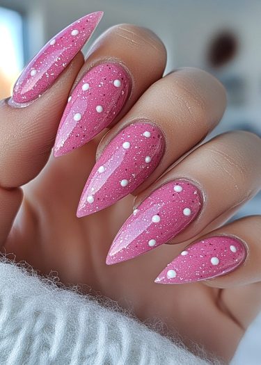 Stylish vibrant pink stiletto nails with white polka dots and glitter sparkle for trendy nail art.