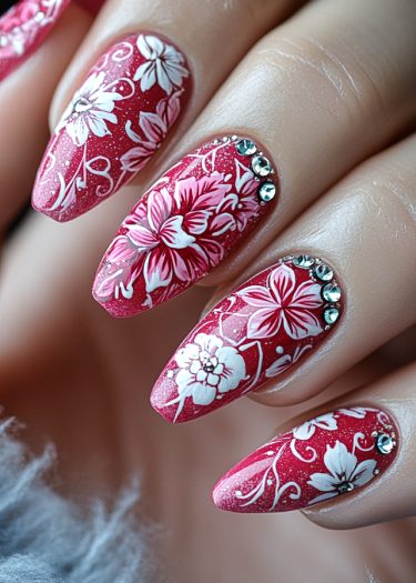 Vibrant cherry red stiletto nails adorned with intricate floral designs and sparkling rhinestones.