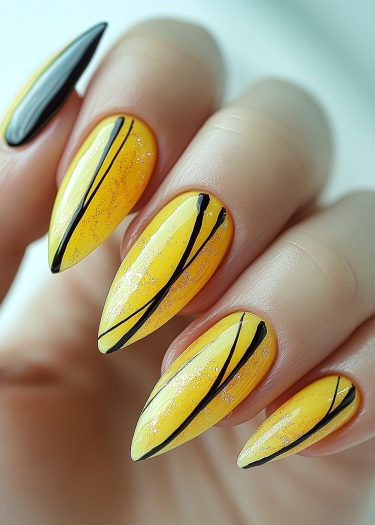 Elegant yellow almond-shaped nails with black designs and glitter for stunning nail art.