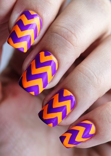 Vibrant zigzag nail art in orange and purple on a well-manicured hand.