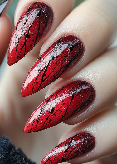 Striking red stiletto nails with artistic black splatter and sparkling silver glitter.