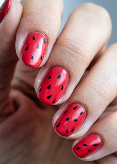 Vibrant red watermelon nail art with black seed designs on beautifully manicured almond-shaped nails.