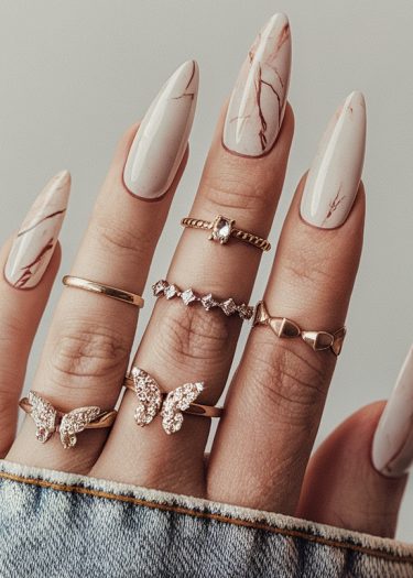 Elegant white marbled stiletto nails with statement rings, blending glamor and casual style.