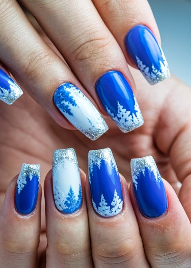 Stunning blue and white winter nail art featuring snow tree designs and glittery silver tips.