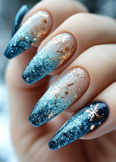 Intricate winter-themed gradient nails with gold snowflakes and glitter on a glossy finish.