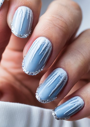 Elegant winter icy nail designs featuring blue polish, intricate white patterns, and sparkling silver tips.