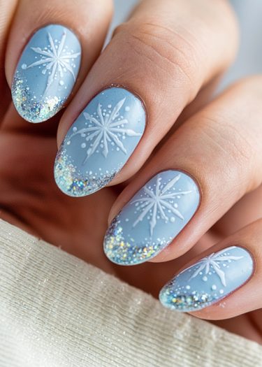 Elegant winter nail art featuring pastel blue base and intricate snowflake designs with glitter tips.