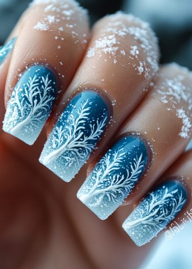 Elegant winter ombre nail art featuring blue and white tree designs and sparkling snowflakes.