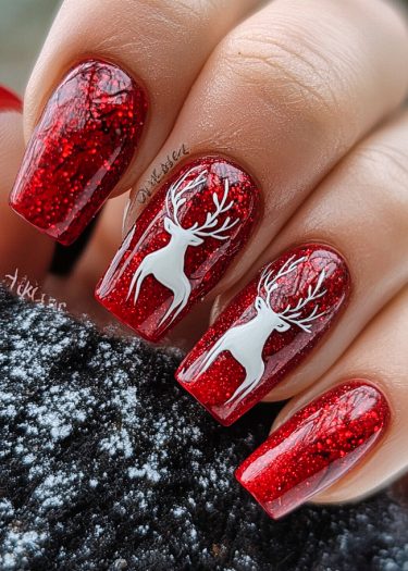 Festive red glitter nails with white reindeer art, perfect for winter holiday celebrations.