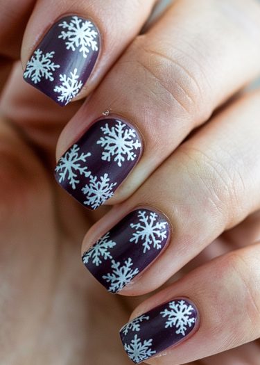 Elegant winter nail art featuring dark purple nails with intricate white snowflake designs.