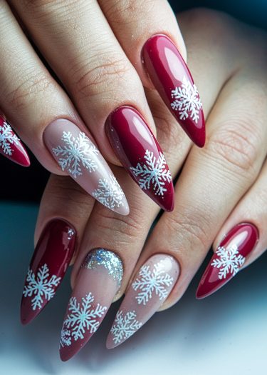 Elegant winter snowflake nail art with vibrant red and nude pink designs on elongated almond nails.