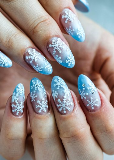 Stiletto nails with winter snowflakes and a blue gradient for festive nail art.