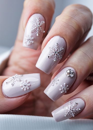 Elegant winter snowflake nail art with pink polish and sparkling rhinestones.