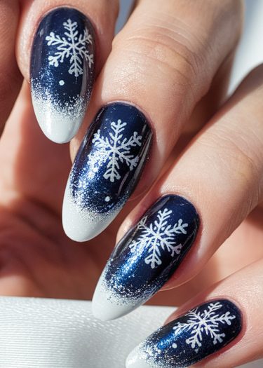 Elegant winter snowflake nail art on deep navy blue almond-shaped nails with glossy finish.