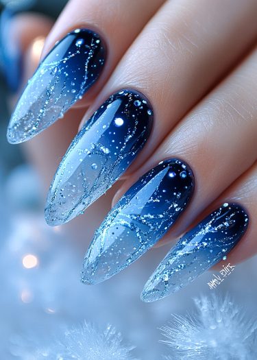 Elegant winter-themed ombré nails with intricate silver glitter patterns and icy blue hues.